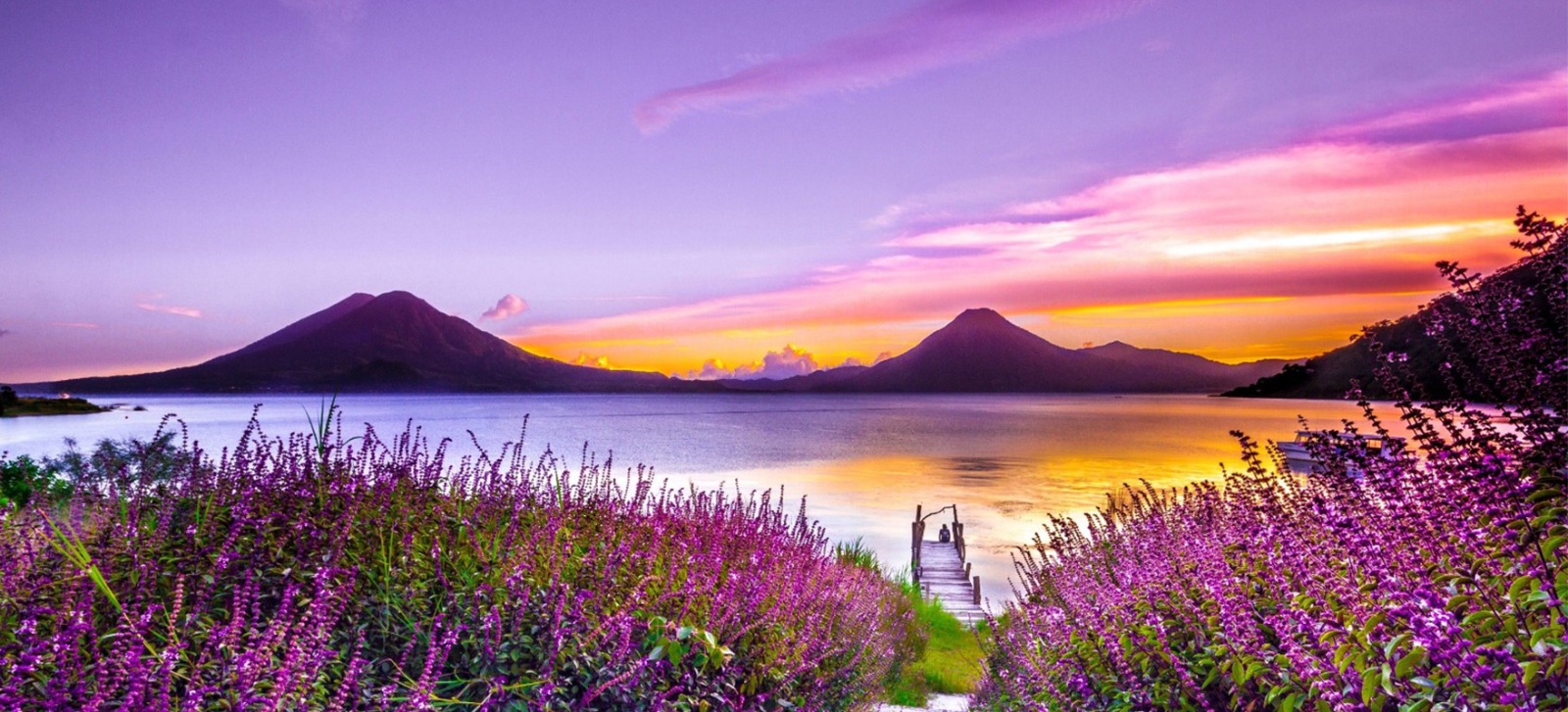 Apus violet peste un lac de munte, cu un ponton de lemn printre flori