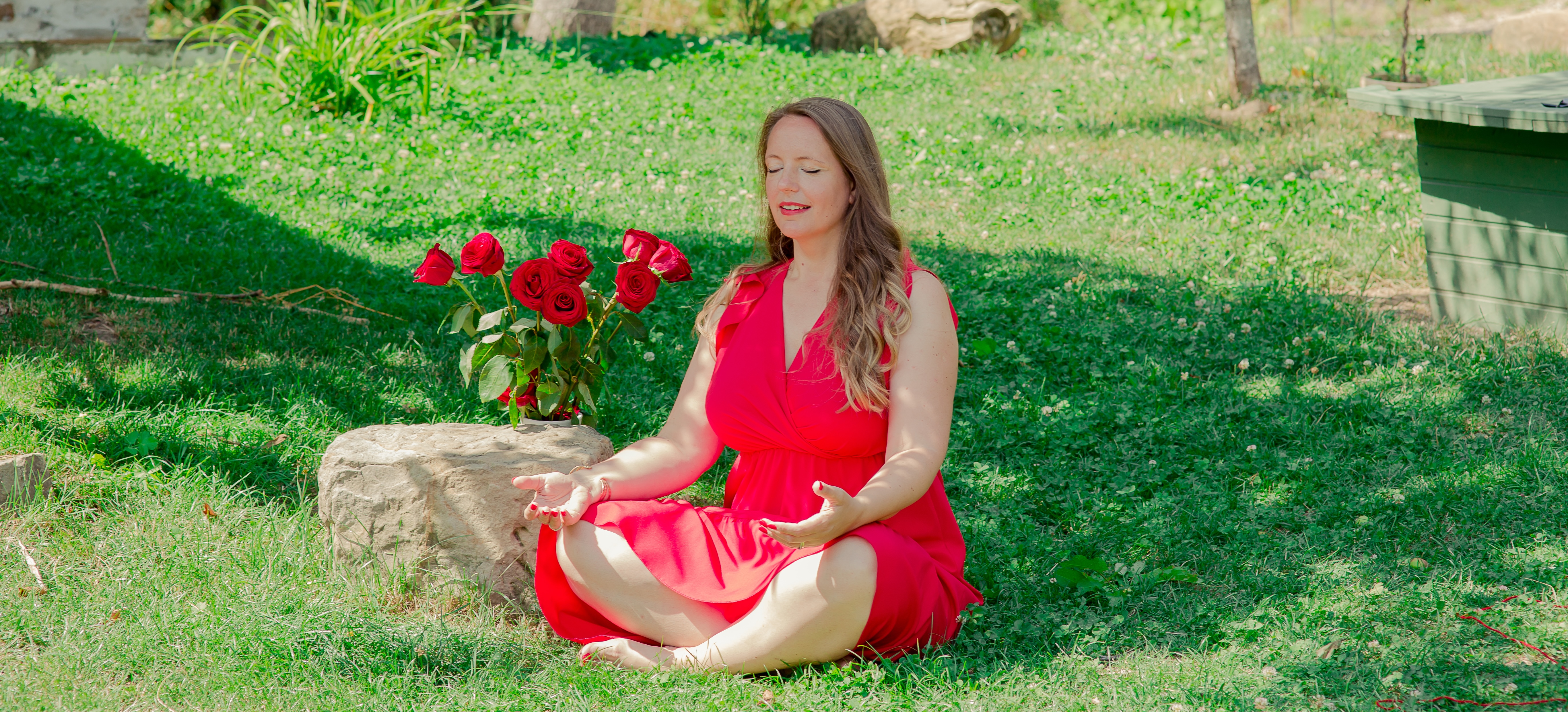Bianca Varvara meditând în iarbă, cu palmele deschise, lângă un buchet de trandafiri roșii